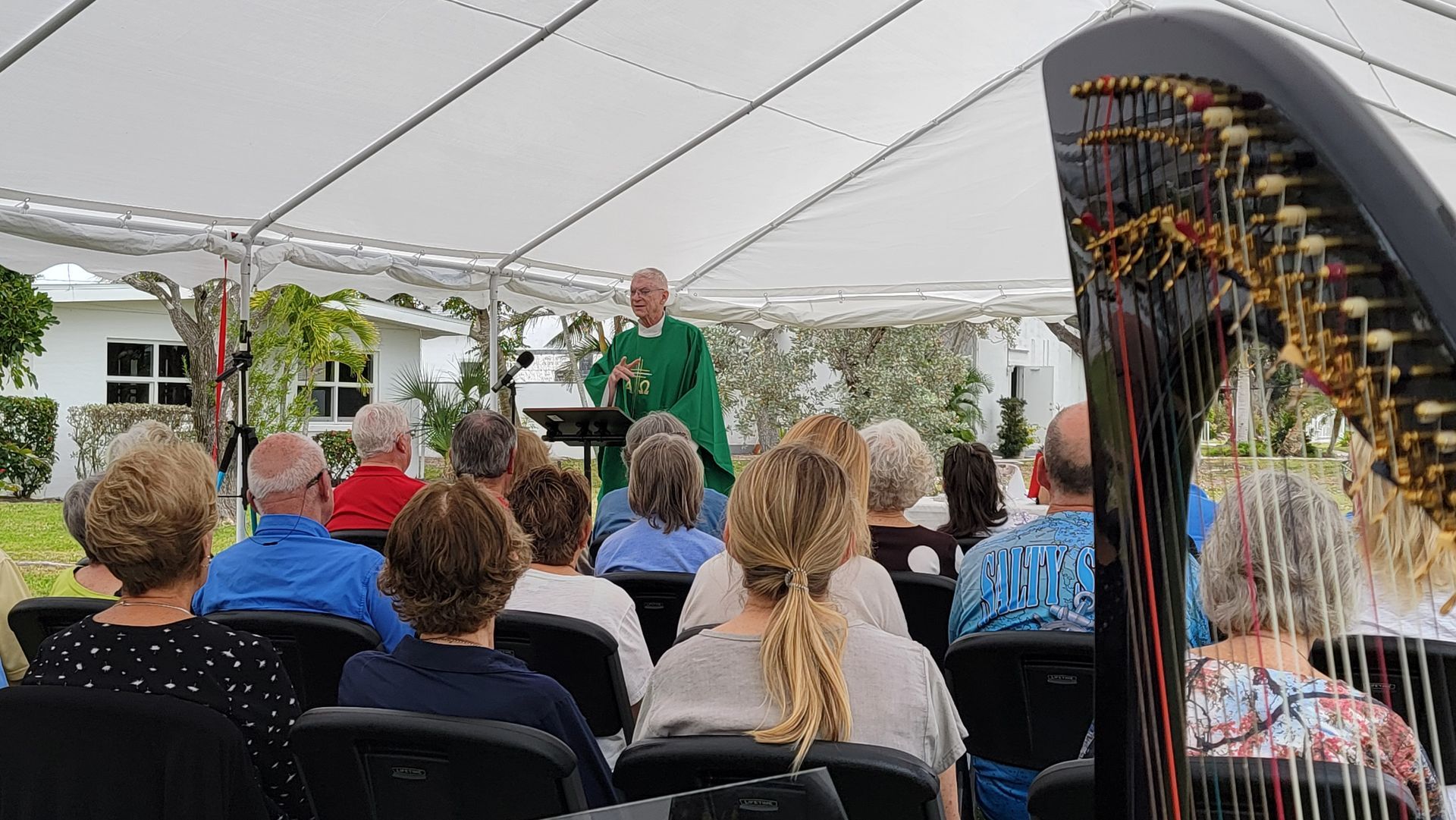 A priest preaching under a tent to an audience, with a harp in the foreground.