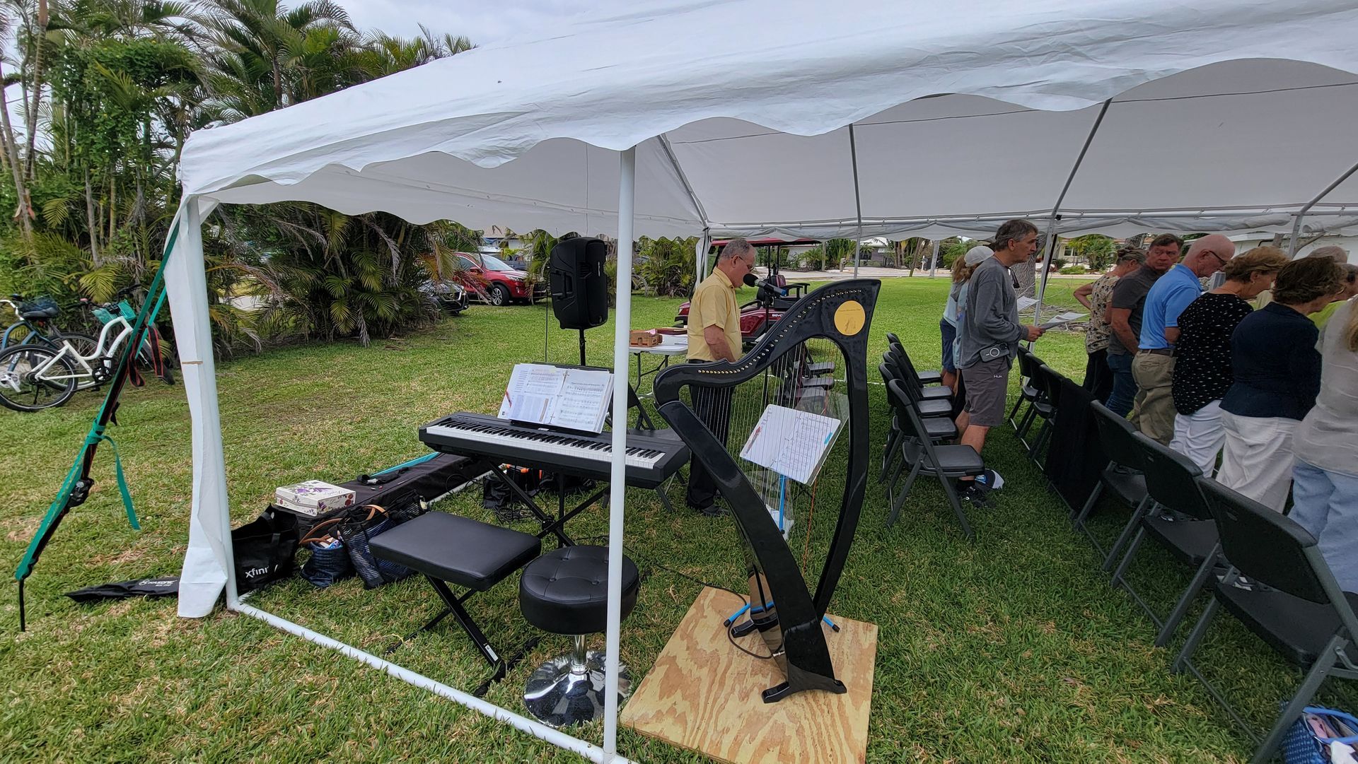 A band playing under a white tent on grass with an audience of people.