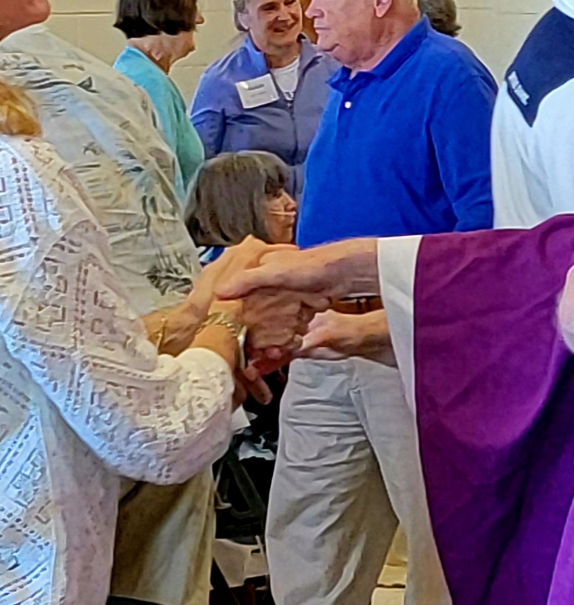 People praying together, hands joined. One woman appears to be frail; others are smiling.
