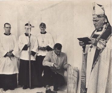 A group of priests are standing around a man kneeling down