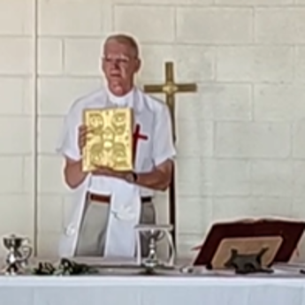 A man in a white robe is holding a bible in front of a cross.