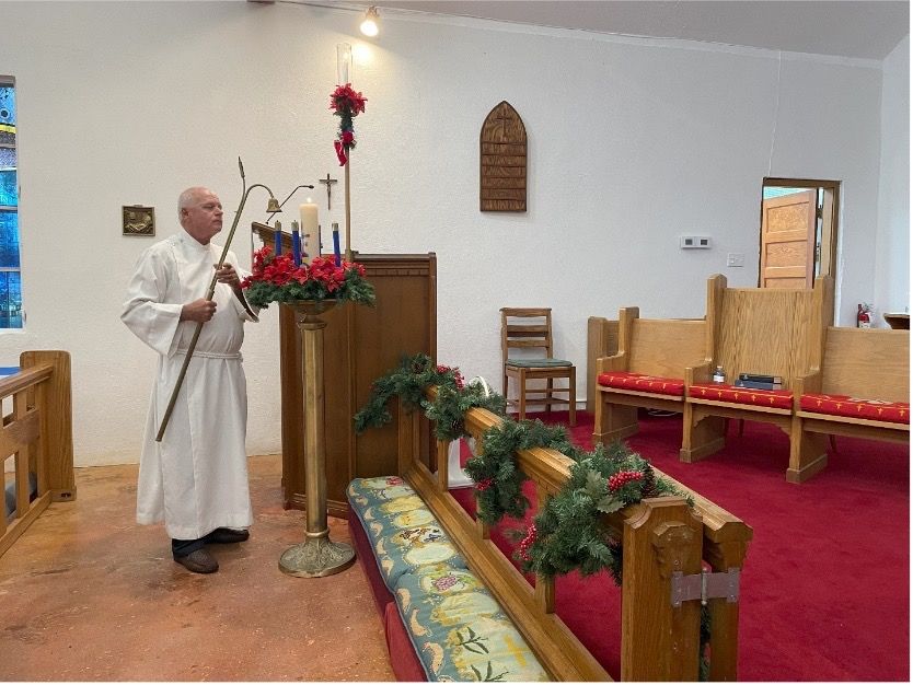 A man in a white robe is standing in a church holding a cane.