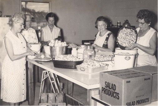 A group of women are preparing food in front of a box that says salad products