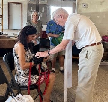 A man is petting a dog while a woman sits in a chair