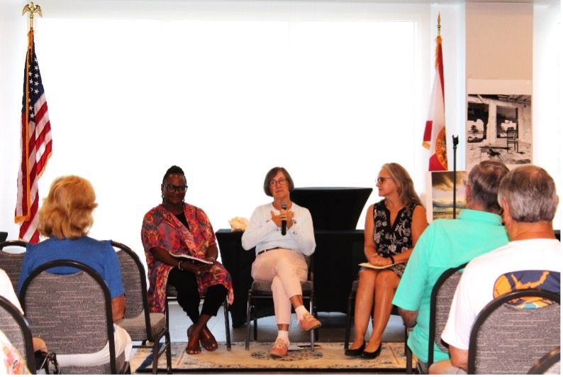 A group of people are sitting in chairs in front of an american flag.