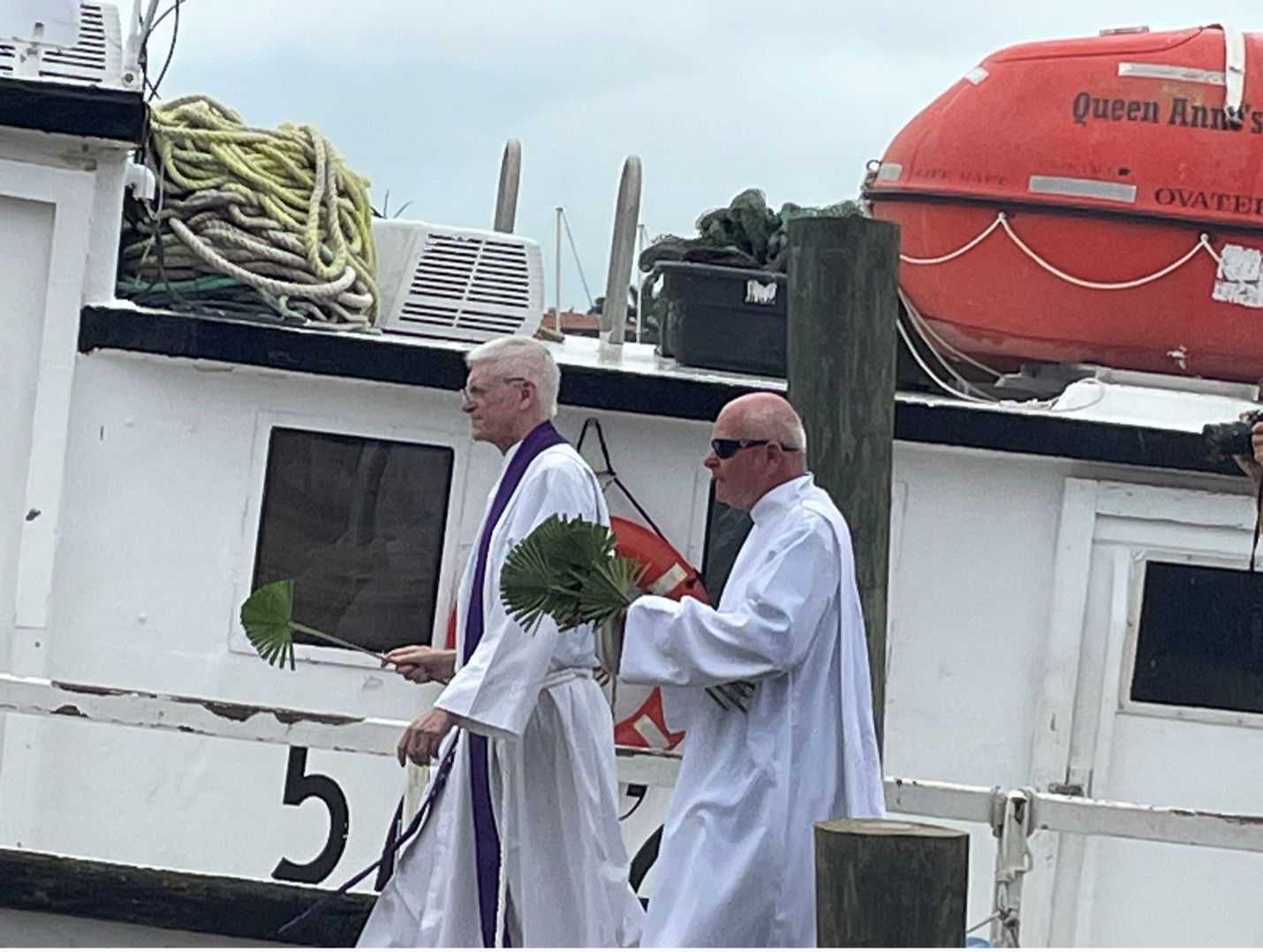 Two priests are walking in front of a boat with the number 5 on it