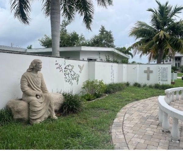 A statue of jesus is sitting on a rock in front of a white wall.