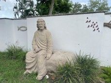 A statue of jesus is sitting on a rock in front of a white wall.