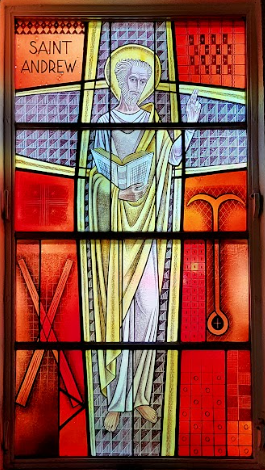 Stained glass window of Saint Andrew on a cross. Red and yellow with the saint holding a book.