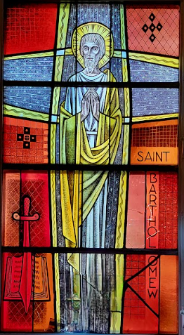 Stained-glass window of St. Bartholomew. Figure in white and gold robes; red and blue background; text 