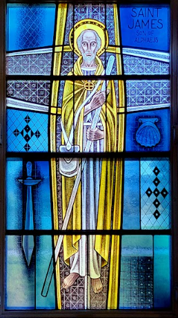 Stained glass window of Saint James in a golden robe, holding staff and sword. Blue background with symbols.
