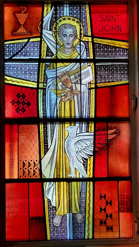 Stained glass window of Saint John, holding a book and pen, with a dove and chalice.