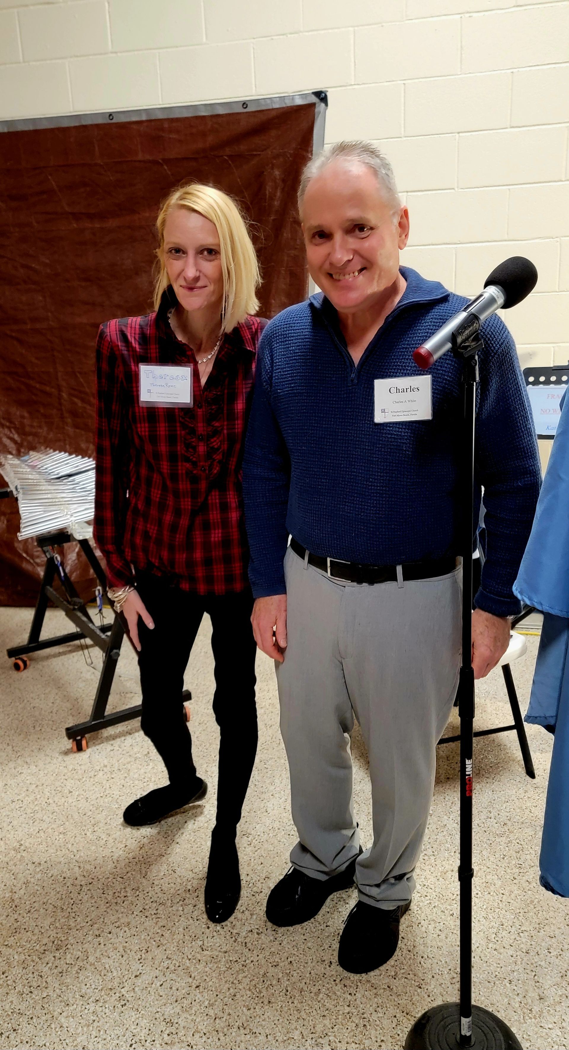 Woman in red plaid and man in blue, smiling at event, posing near a microphone.