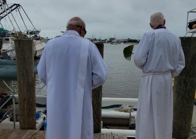 Two men in white robes are standing on a dock looking at the water.