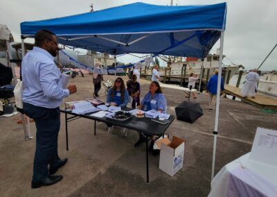 A man is standing in front of a table under a blue tent.
