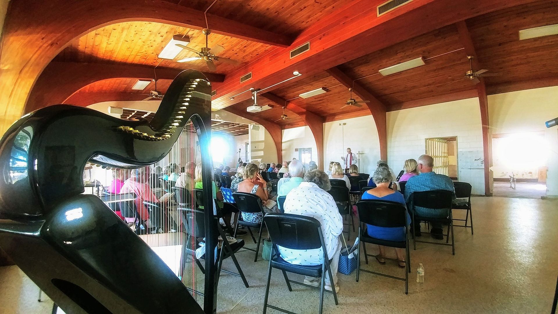 A group of people are sitting in chairs in a large room with a harp in the foreground