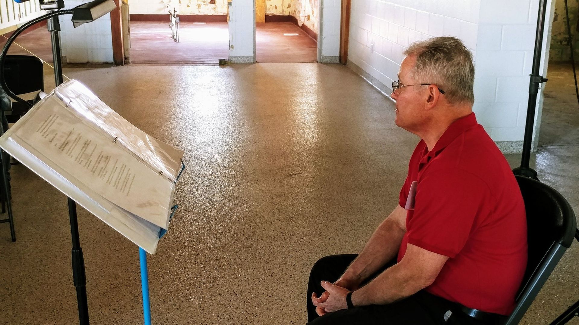 A man in a red shirt is sitting in front of a music stand