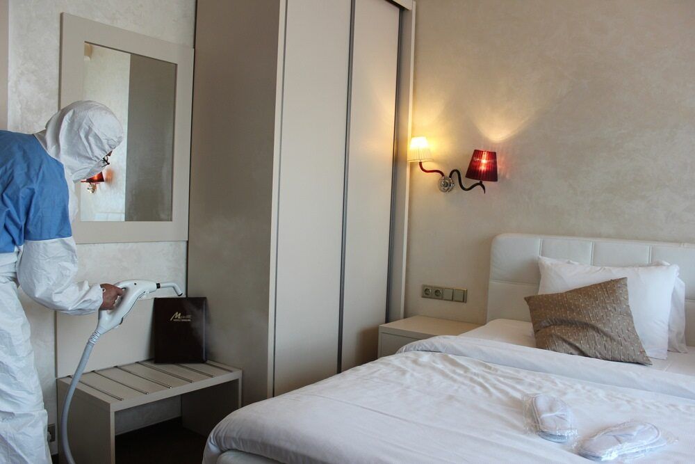 Person in Protective Suit Sanitizing a Hotel Room With Spray — McMahon Pest Services In Bentley Park, QLD