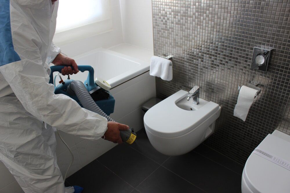 Person in Protective Suit Disinfecting a Bathroom With a Spray Gun — McMahon Pest Services In Bentley Park, QLD