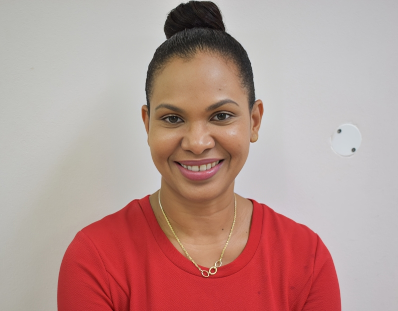 A woman wearing a red shirt and a gold necklace smiles for the camera
