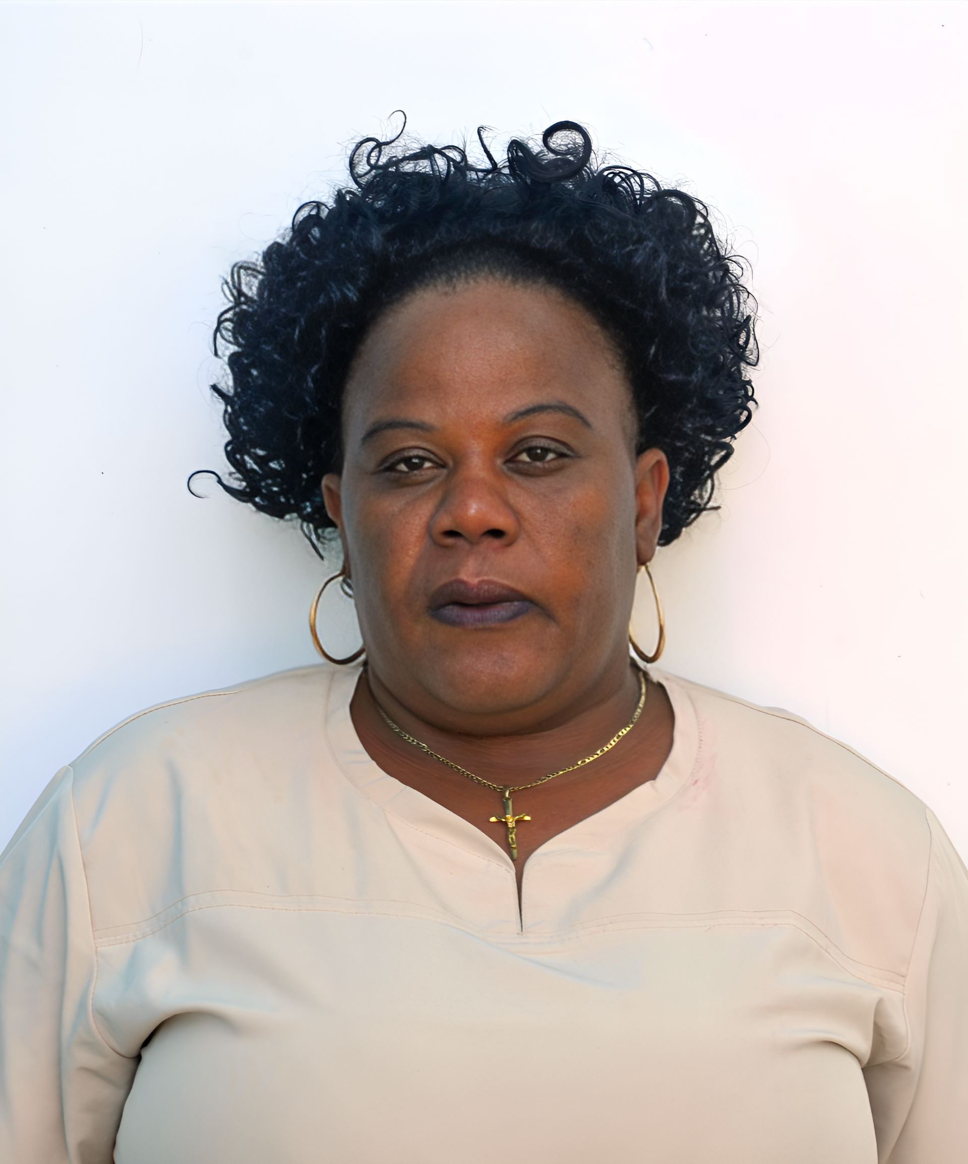A woman with curly hair is wearing a white shirt and gold hoop earrings