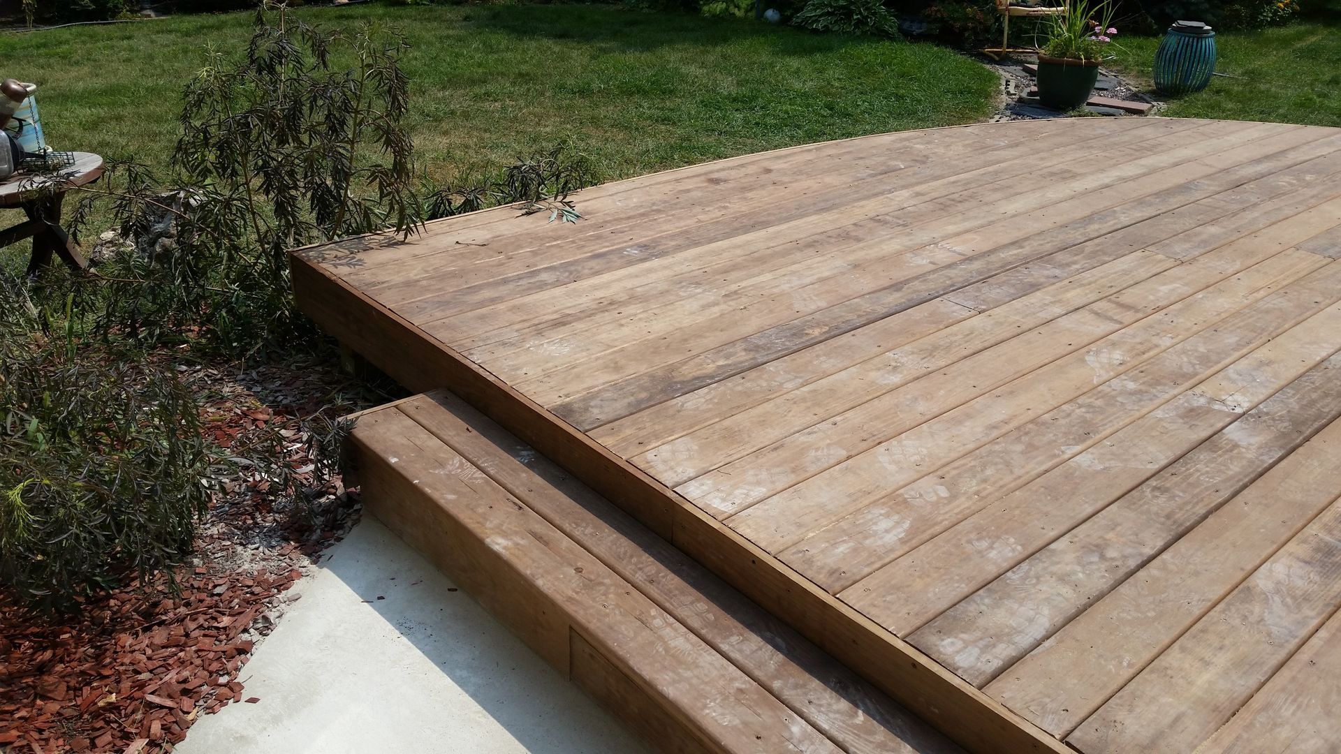 A wooden deck with stairs leading up to it in a backyard.