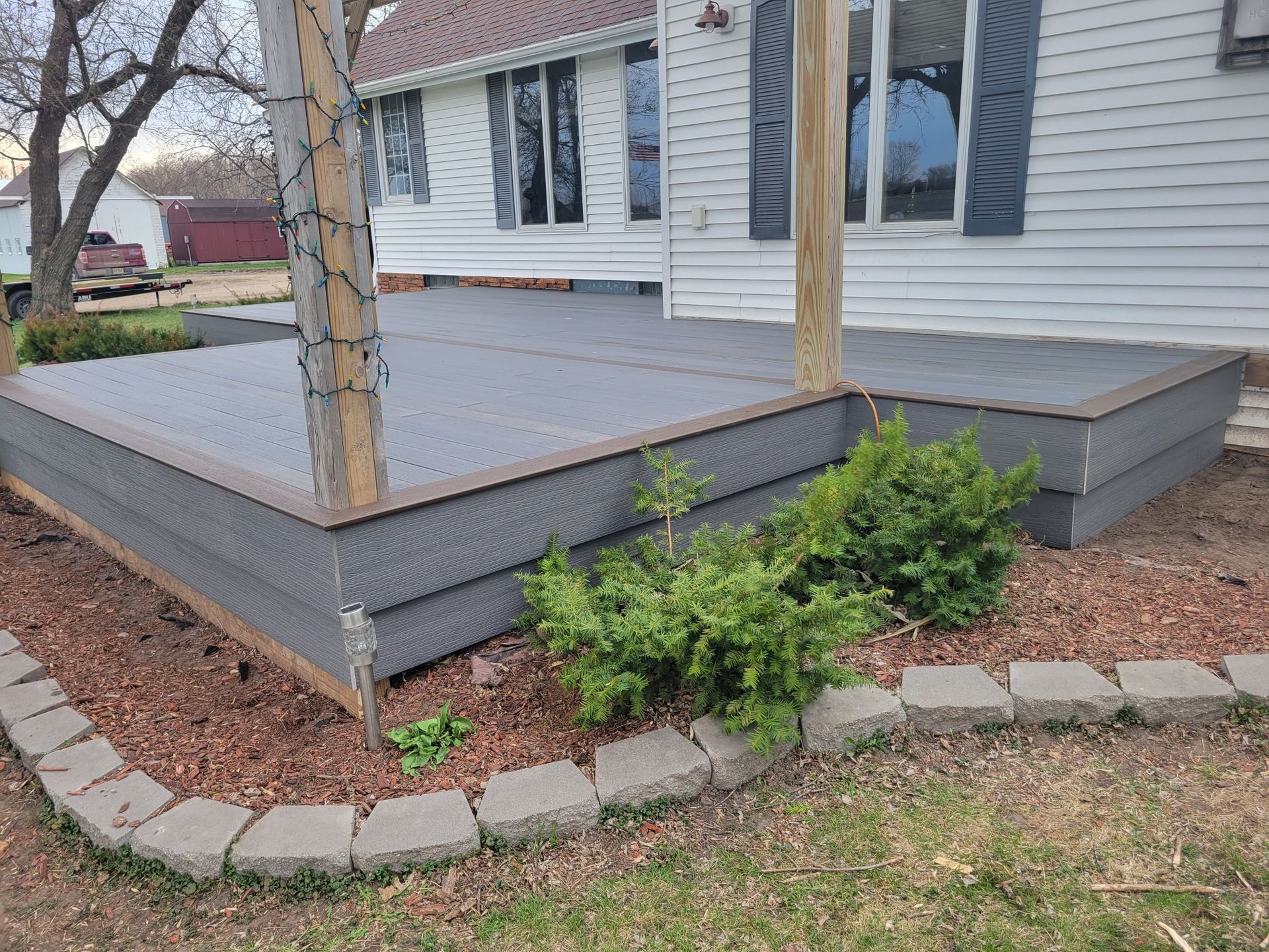 A gray deck is in front of a white house.