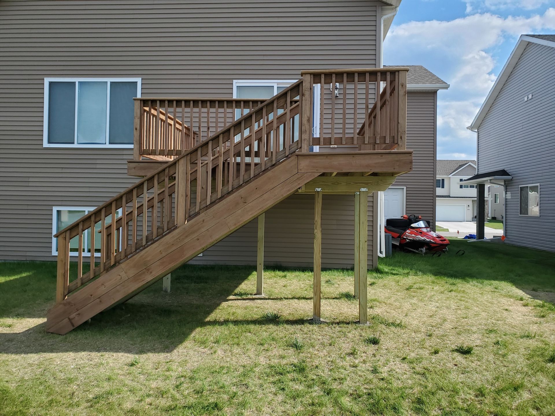 A wooden deck with stairs leading up to it is in the backyard of a house.