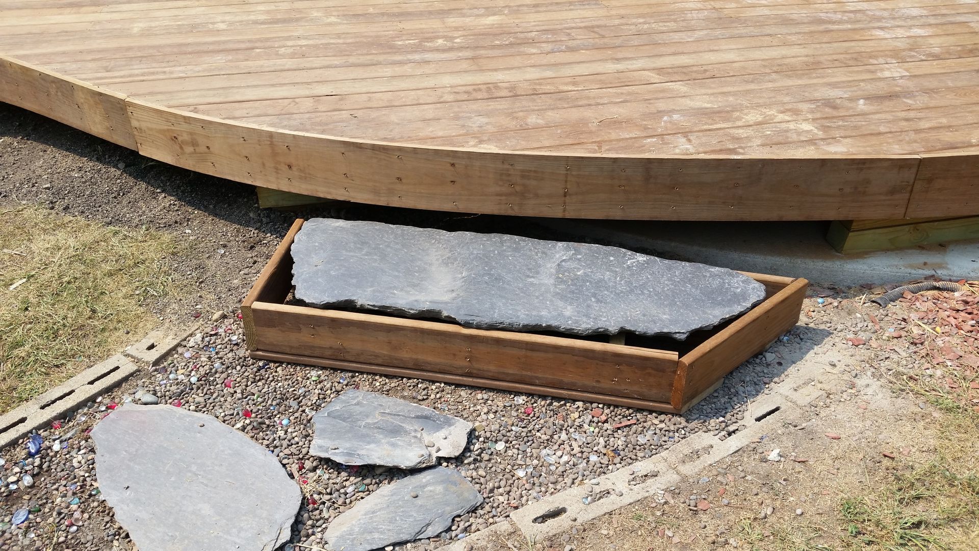 A large rock is sitting in a wooden box on the ground next to a wooden deck.
