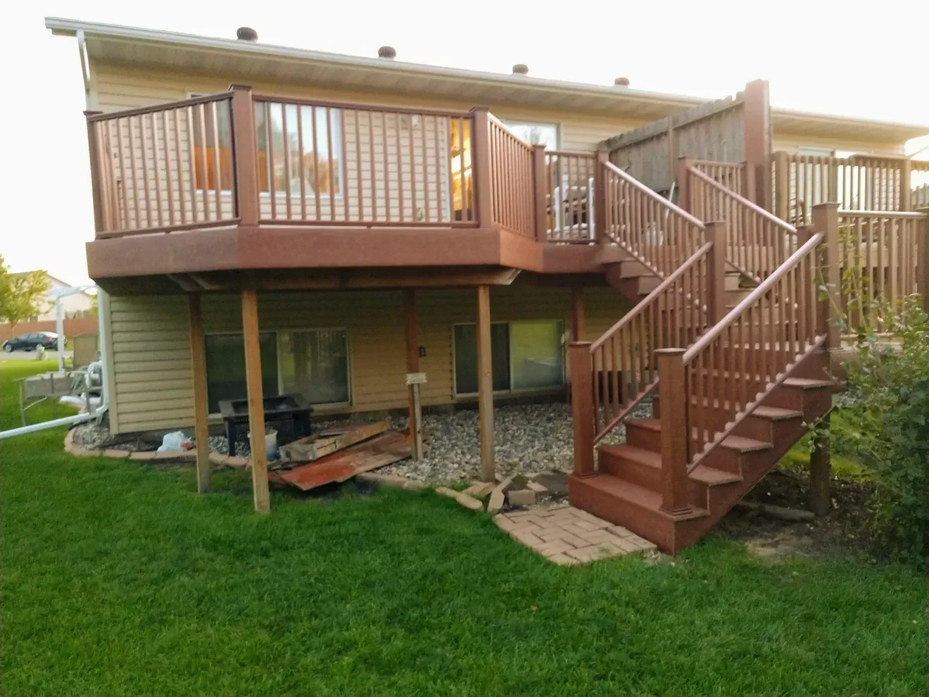 A large deck with stairs leading up to it is in the backyard of a house.