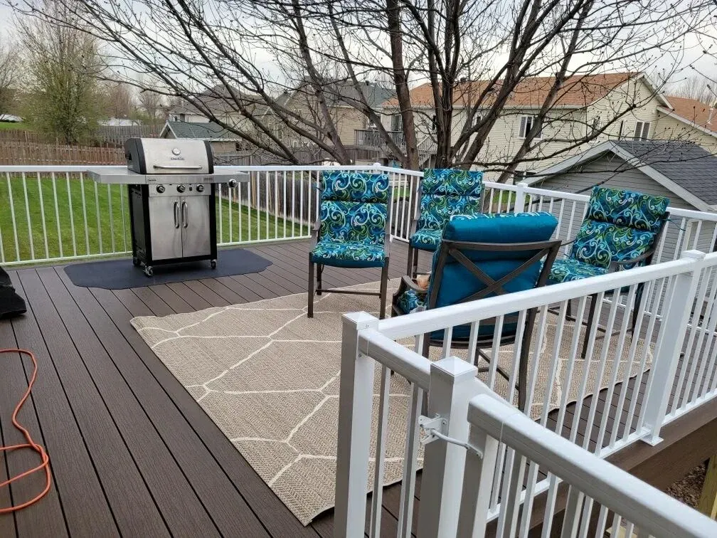 A deck with a grill and chairs on it.
