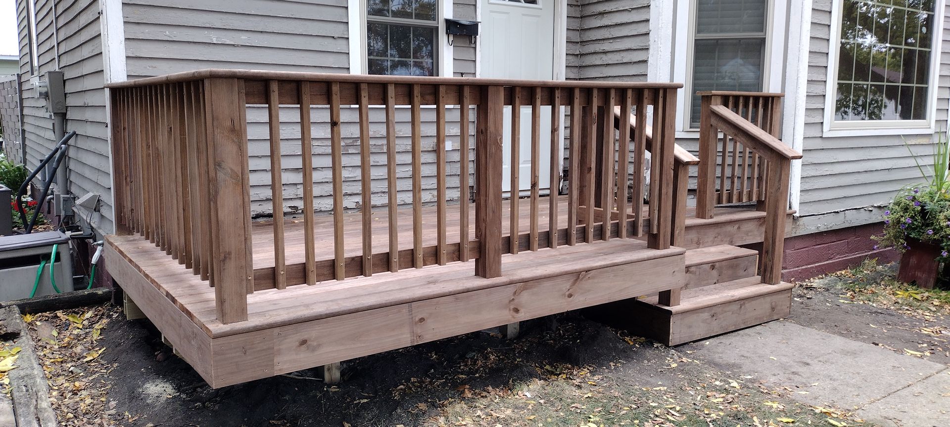 A wooden deck with stairs is in front of a house.