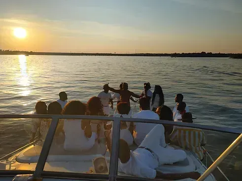 A group of people are sitting on a boat in the water at sunset.