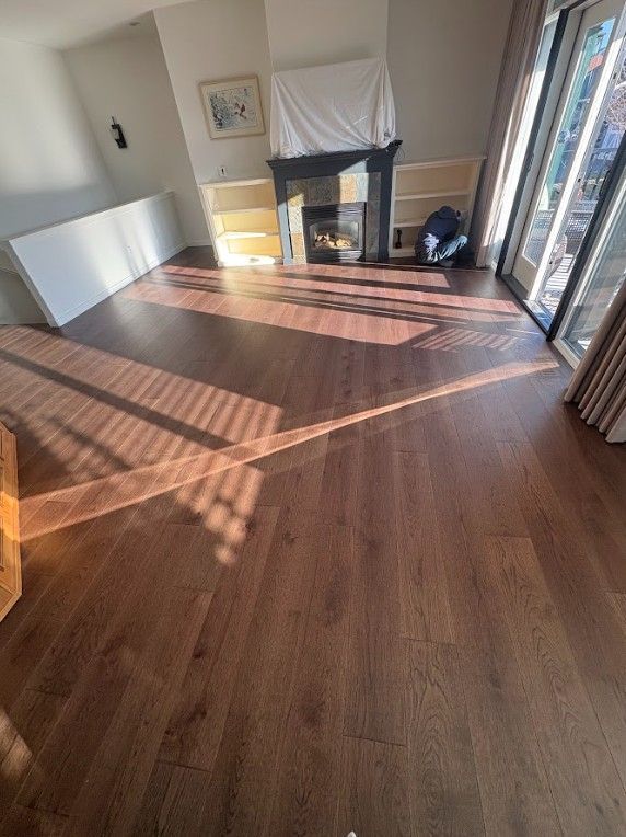 Wooden floor in a room with a fireplace, natural light, and partially installed trim.