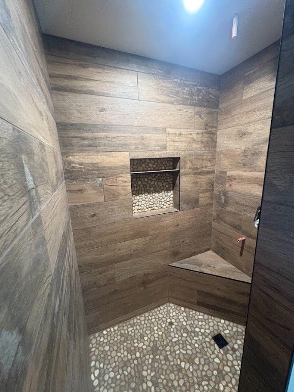 Wood-look tiled shower with a pebble floor, built-in shelf, and corner seat.