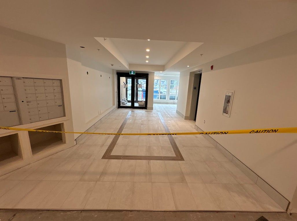 Hallway with light-colored tile flooring, unfinished walls, caution tape, and a mail area. Exterior doors at end.