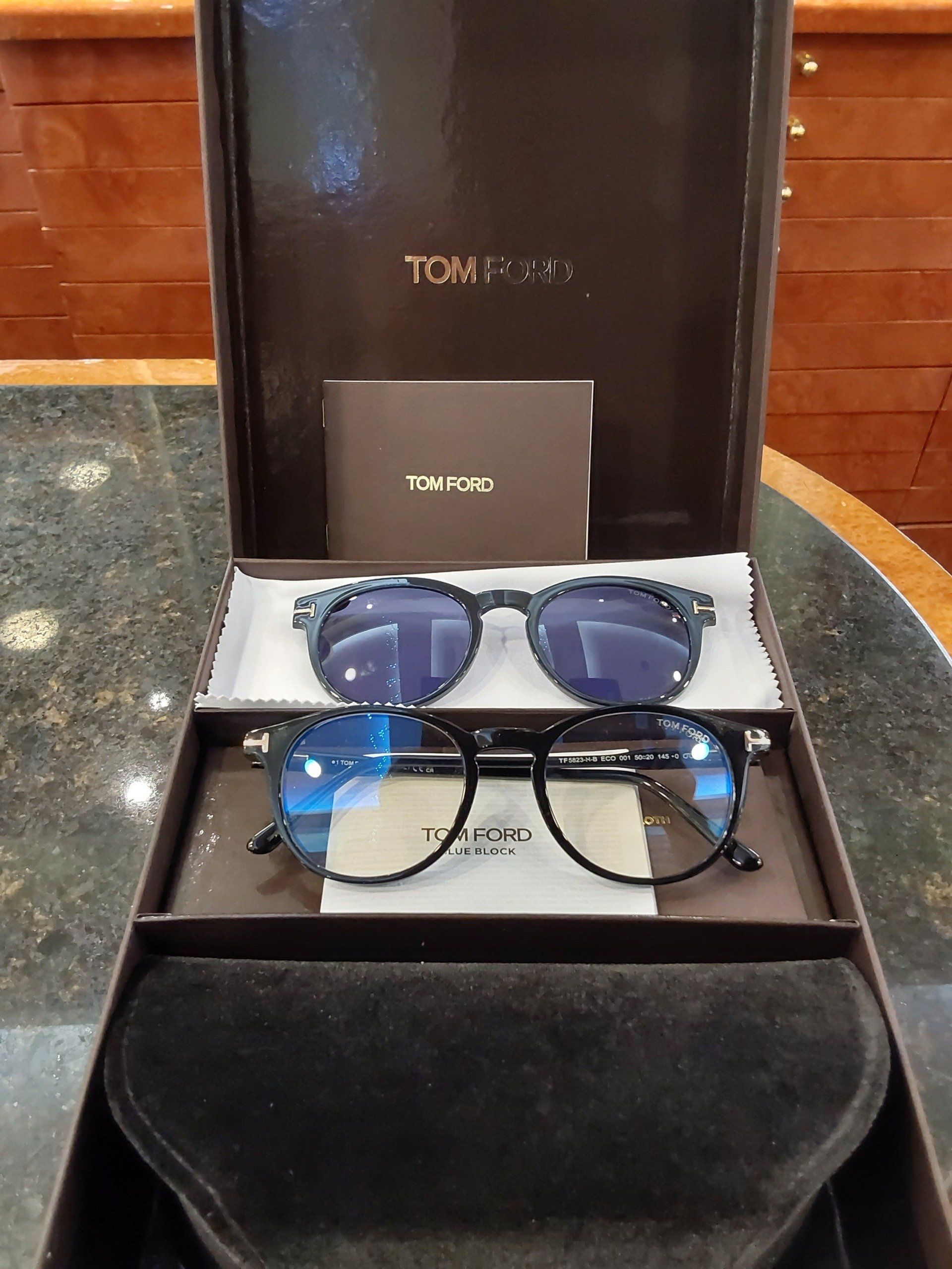 Occhiali da sole Tom Ford in scatola, con custodia marrone scuro, lenti blu e nere.