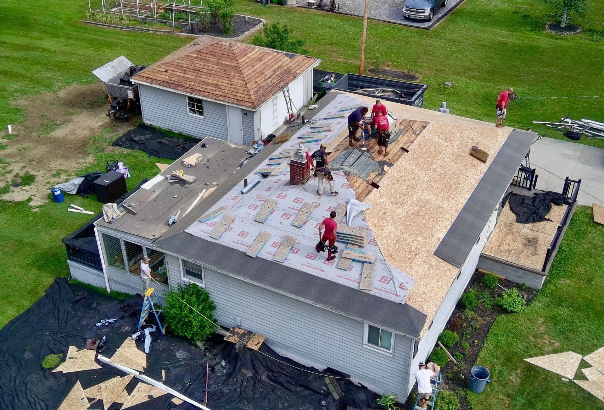 Roofers working on a house roof during a repair or replacement, with shingles removed and materials exposed.
