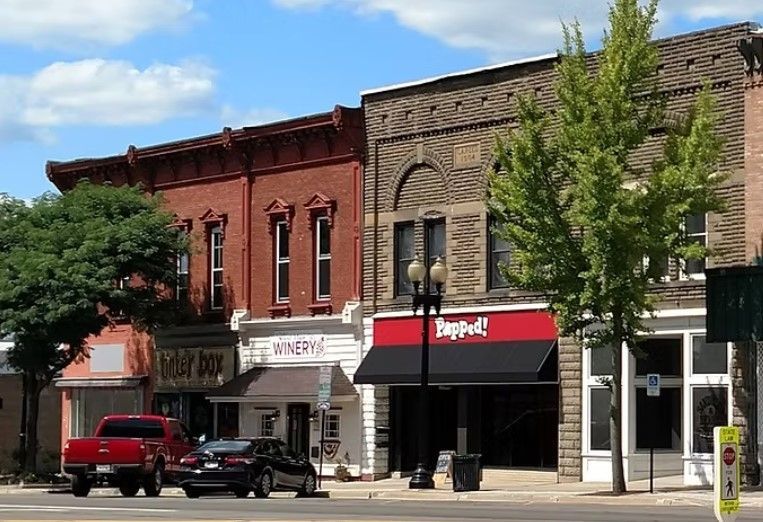 A row of historic brick storefronts in Ravenna, OH on a sunny day with cars parked along the street.