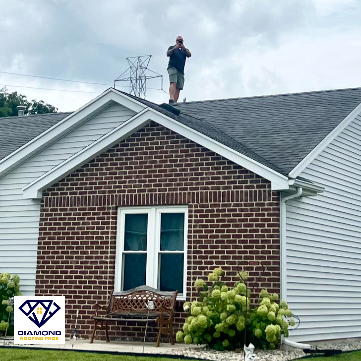 Person standing on a brick house roof with a tool, near a Diamond logo watermark.