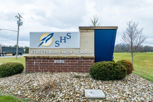 A sign for Streetsboro High School featuring a rocket logo and the school name on a brick base in a grassy, rocky area.