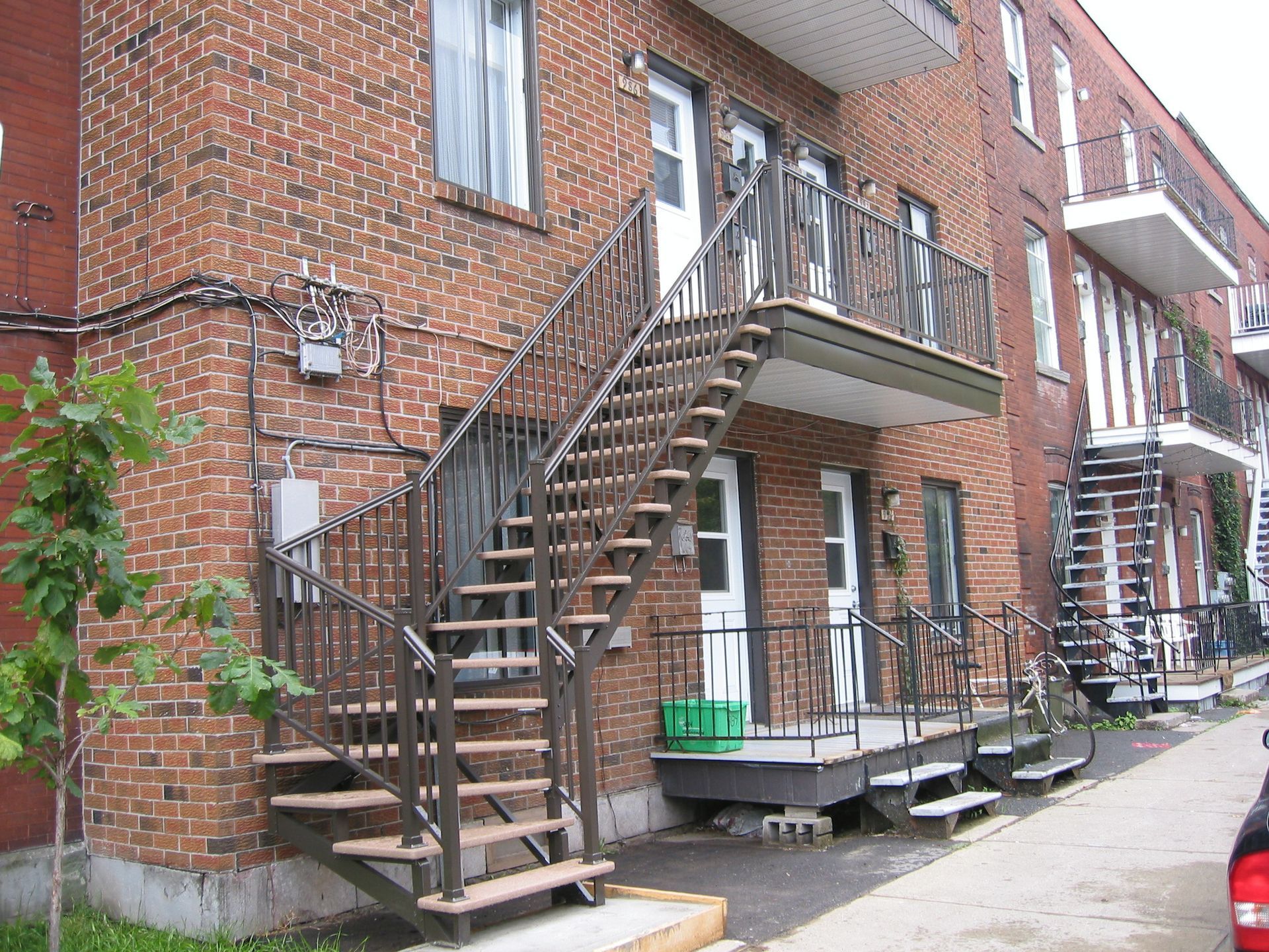 Immeuble d'appartements en briques avec escalier extérieur en métal et petits balcons donnant sur un trottoir.