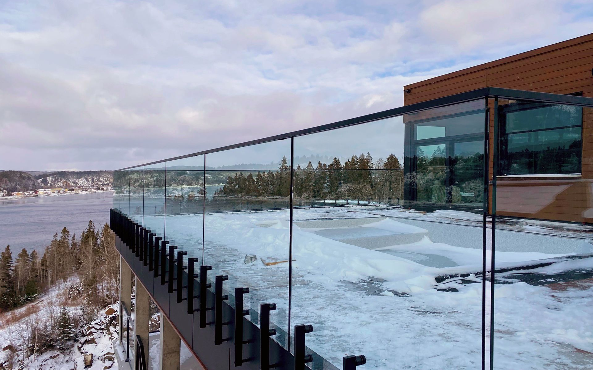 Terrasse enneigée au bord du lac avec balustrade en verre et bâtiment moderne donnant sur l'eau gelée