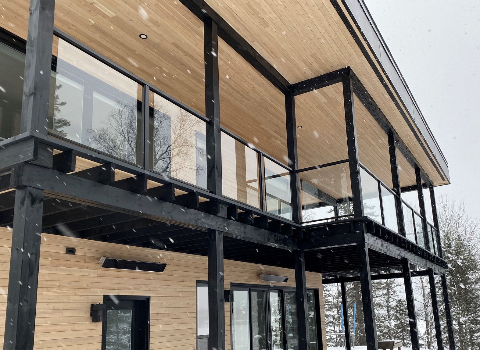 Maison moderne en bois et noir avec balcon à l'étage et grandes fenêtres dans un cadre enneigé