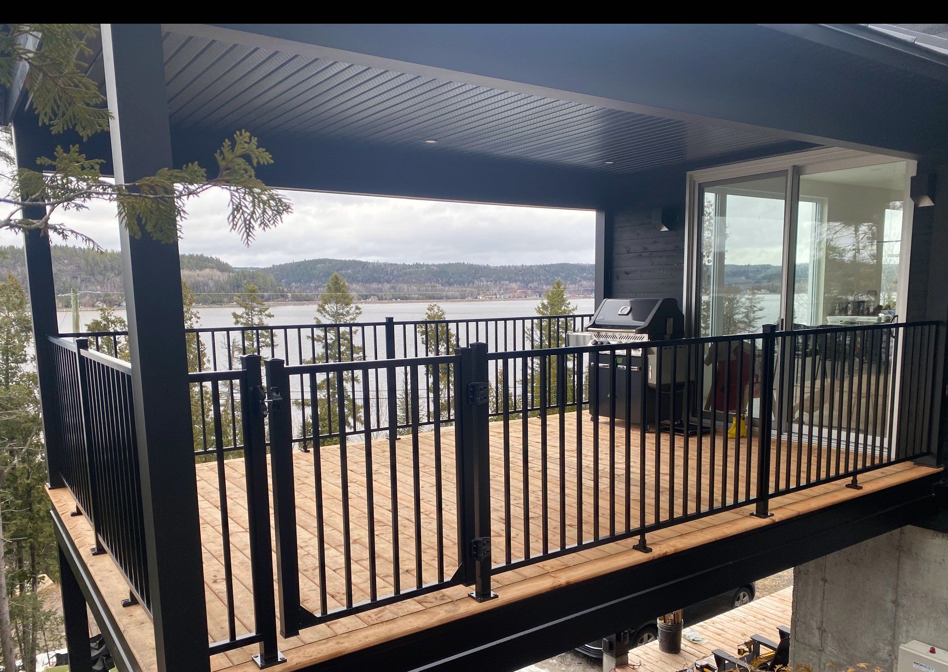 Balcon moderne avec balustrades noires et paroi de verre donnant sur un lac et des montagnes