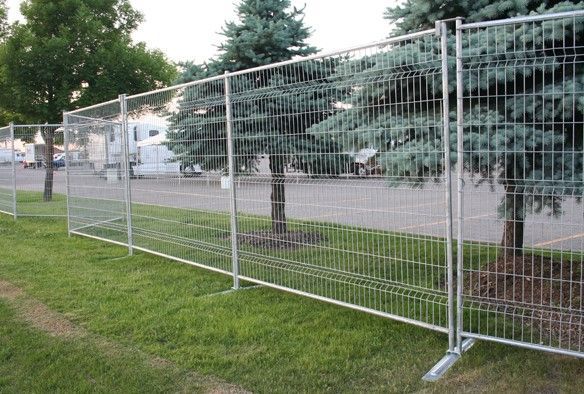 Clôture métallique temporaire le long d'une route herbeuse, près d'arbres et de maisons