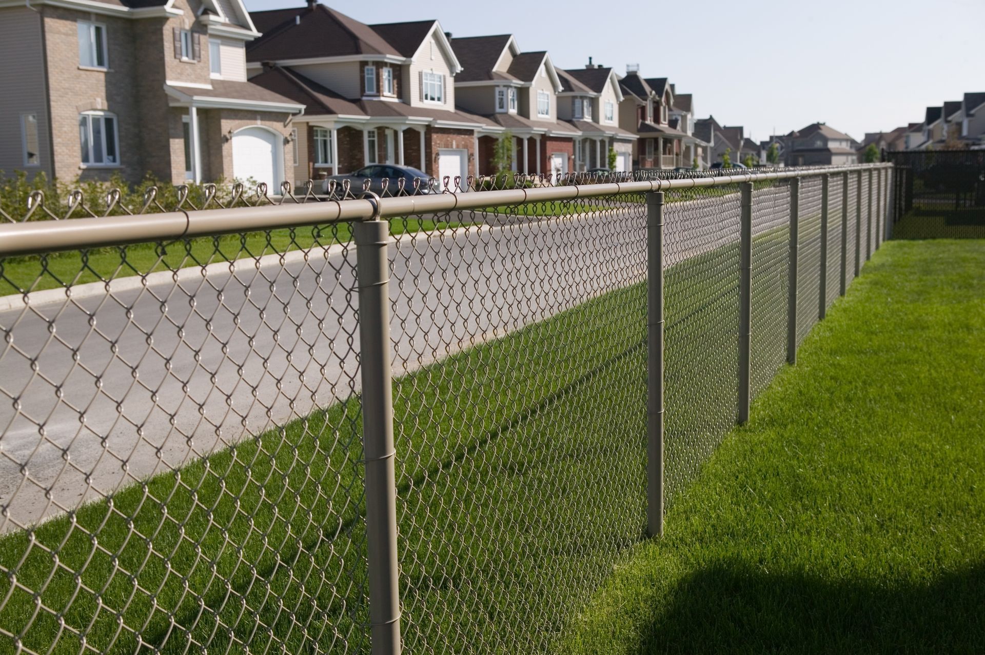 Clôture en grillage bordant une pelouse verdoyante et des maisons de banlieue le long d'une rue