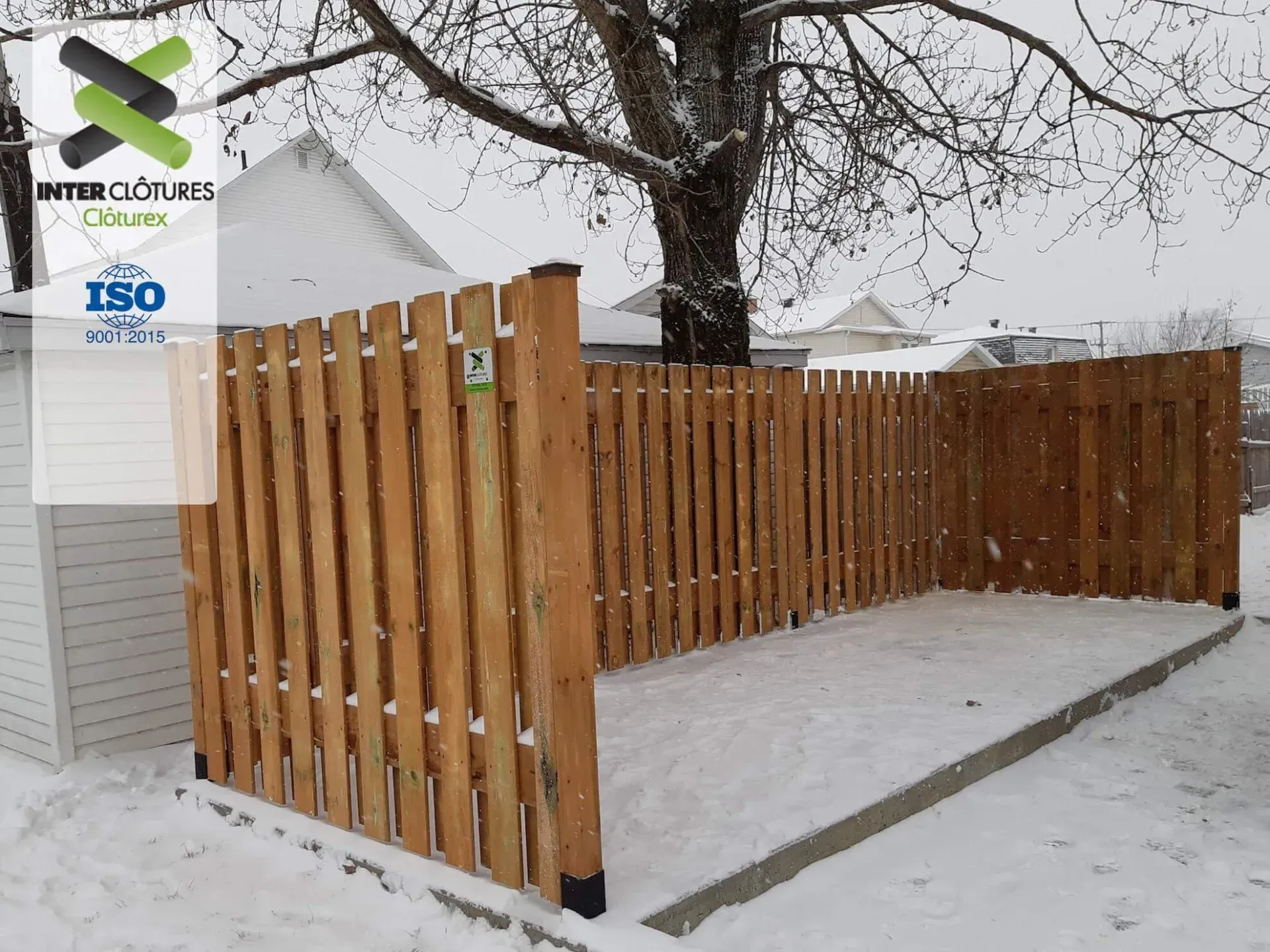 Cour enneigée avec une clôture en lattes de bois à côté d'une maison et d'arbres dénudés