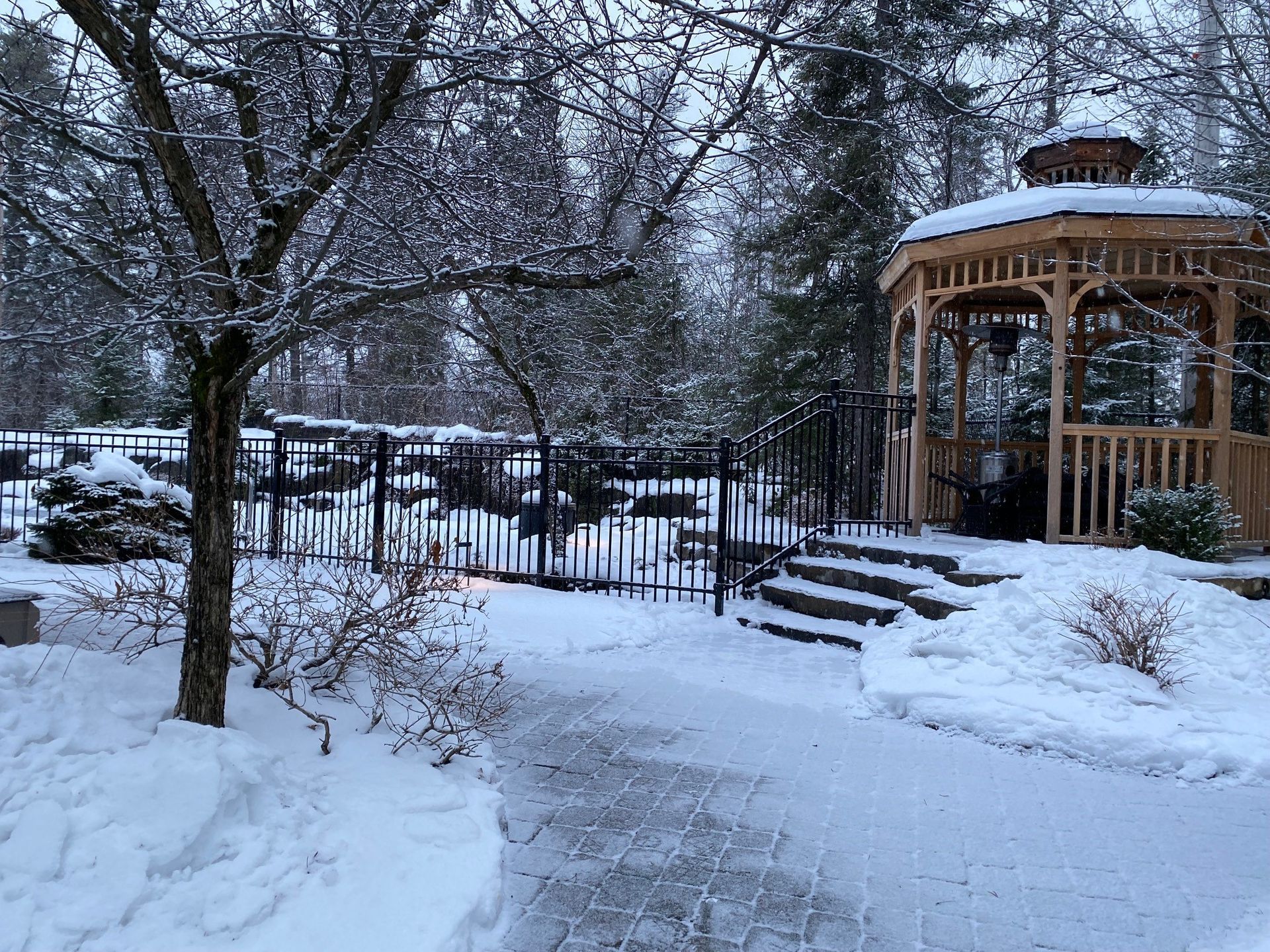 Allée de jardin enneigée menant à un kiosque et à une clôture en fer en hiver.