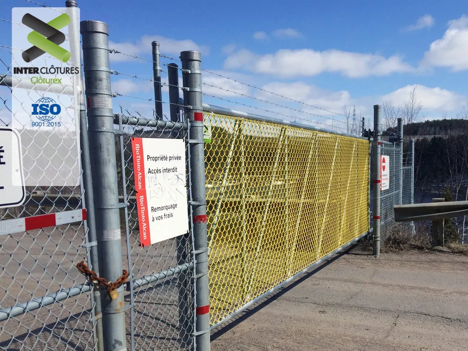 Clôture en grillage autour d'un site industriel, avec panneaux d'avertissement et filet de sécurité jaune.